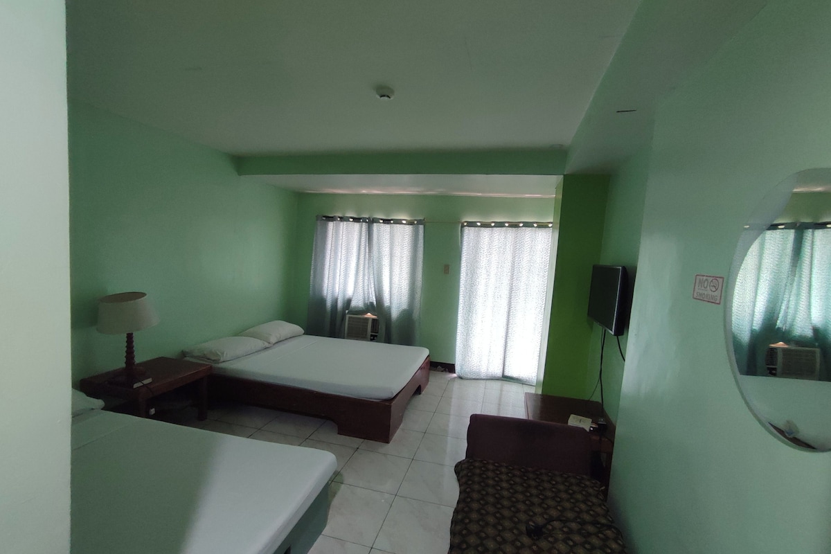 Una habitación de hotel con dos camas individuales, una mesita, una silla, una lámpara, un televisor y un espejo.