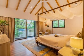 A bedroom with a large bed, a bedside table, a lamp, a window with a view of greenery, and a balcony. - Elivaas Shai - Goa (Assagao)
