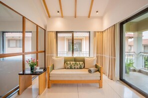 A modern living room with a sofa, a small table with a vase, and large windows with curtains. - Elivaas Shai - Goa (Assagao)