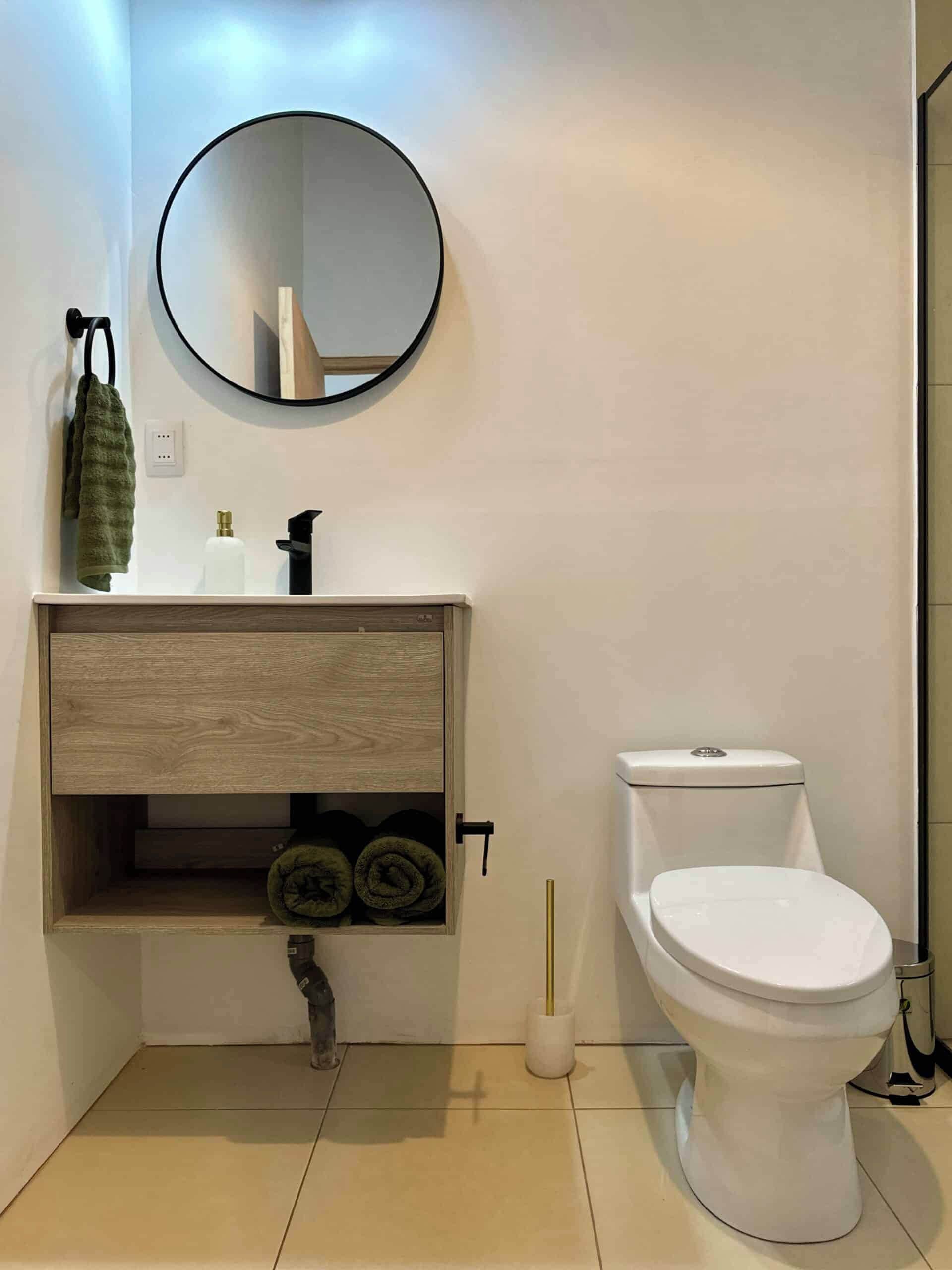 Een moderne badkamer met een houten wastafel, een ronde spiegel, een toilet en een handdoekrek.