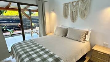 Un dormitorio con cama, mesita de noche, un tapiz de macramé y vistas al exterior.