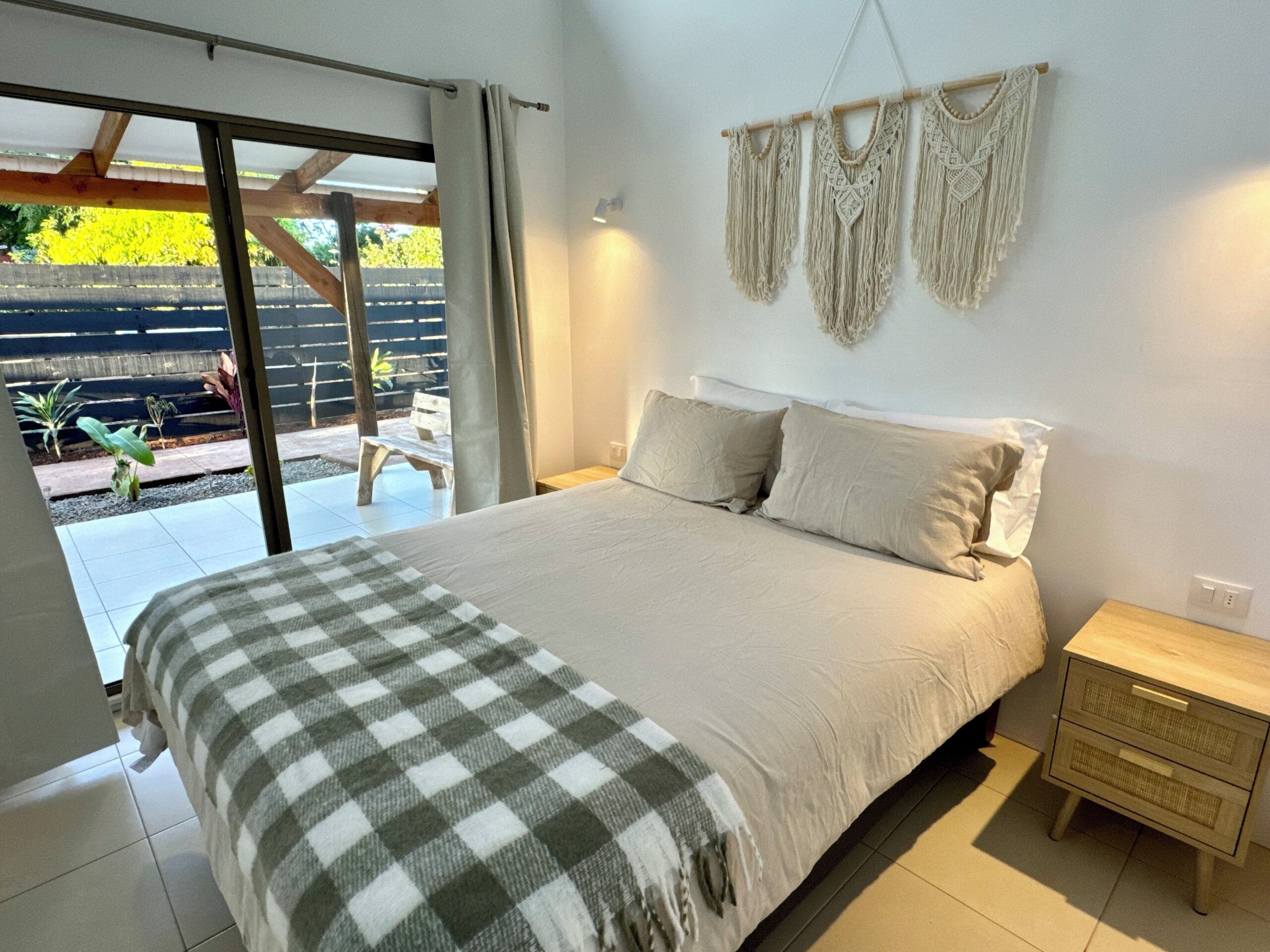 Un dormitorio con cama, mesita de noche, un tapiz de macramé y vistas al exterior.
