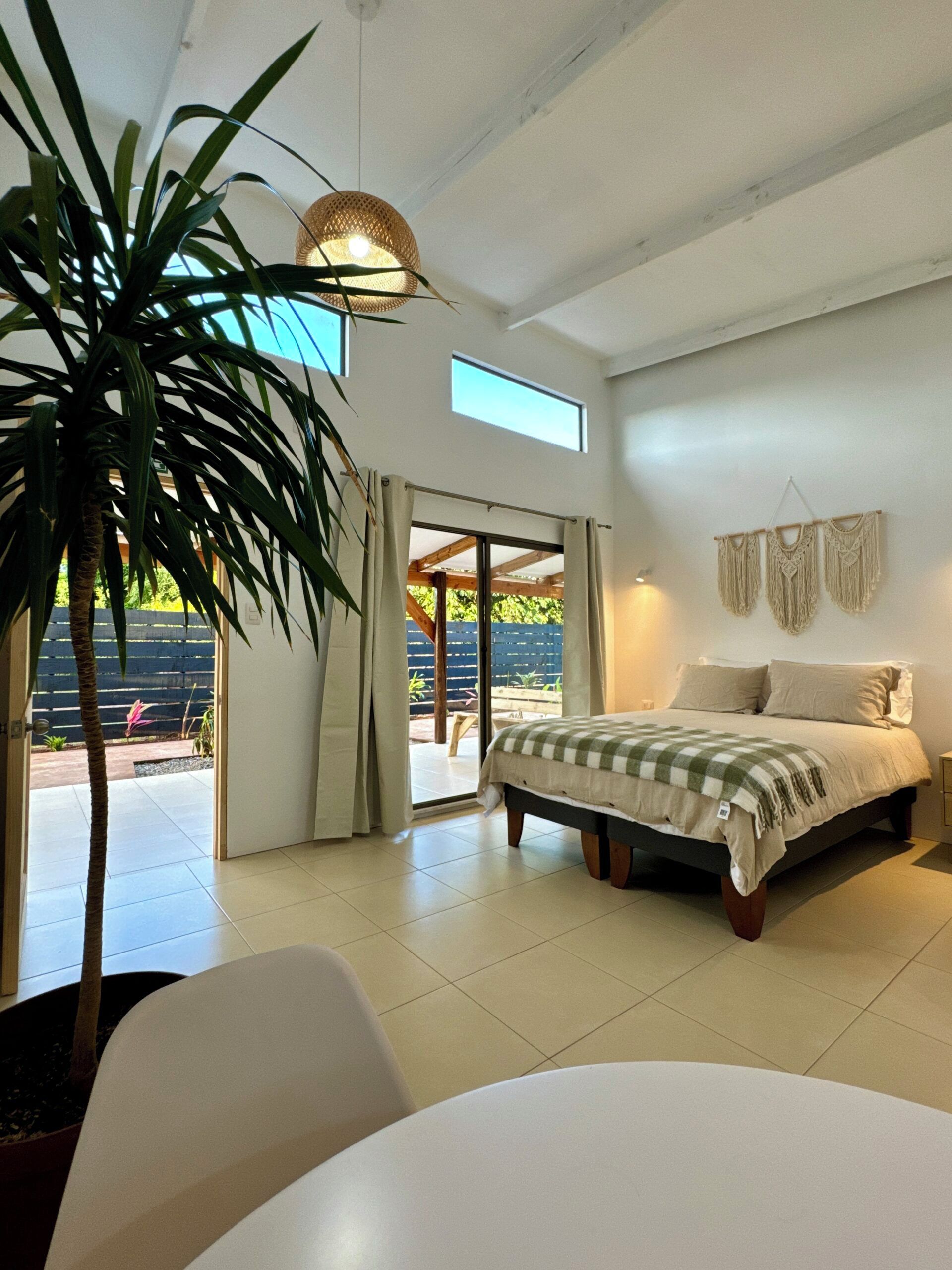 Un dormitorio con cama, una planta grande en maceta, una lámpara de techo y vistas al exterior.