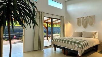 Un dormitorio con cama, una planta grande en maceta, una lámpara de techo y vistas al exterior.