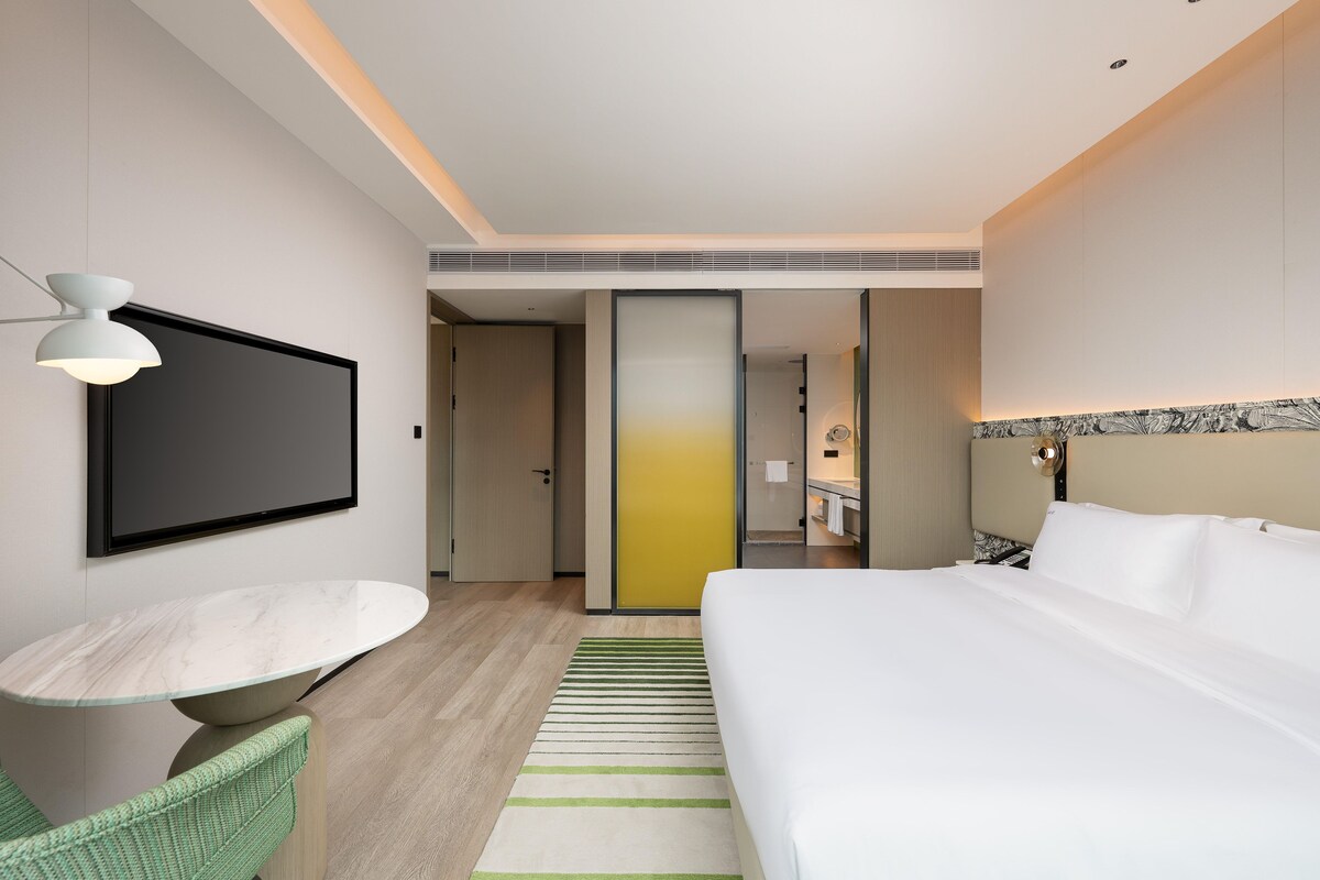 A modern hotel room with a bed, a dining table, and a TV.