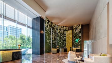 A modern lobby with a reception desk, seating area, and large windows offering views of greenery.