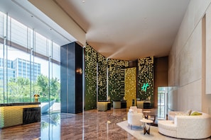 A modern lobby with a reception desk, seating area, and large windows offering views of greenery. - Holiday Inn Fuzhou Exhibition Center (Fuzhou)