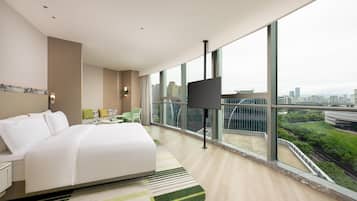 Una habitación de hotel moderna con una cama grande, televisión y balcón con vistas a la ciudad.