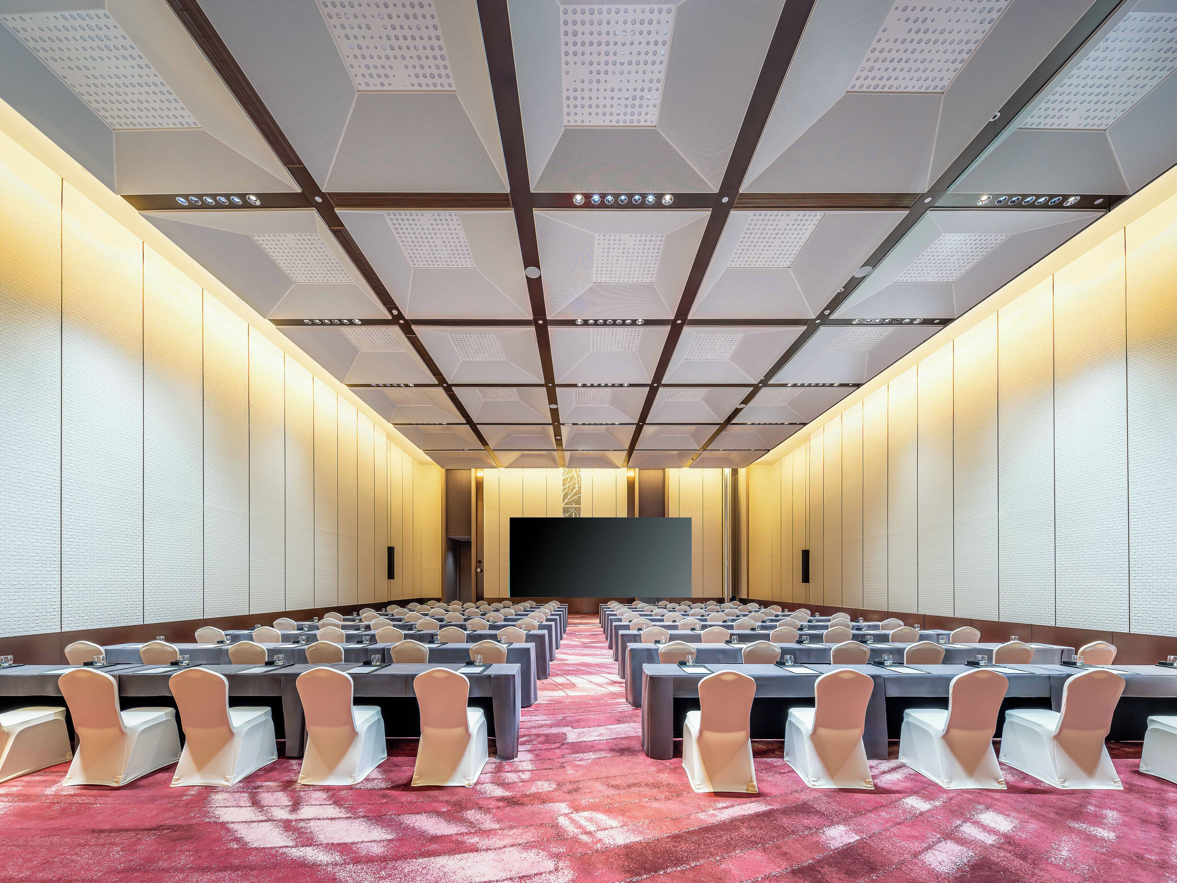 A conference room with tables and chairs, a large screen, and a patterned ceiling.