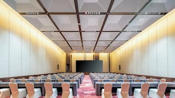 A conference room with tables and chairs, a large screen, and a patterned ceiling.