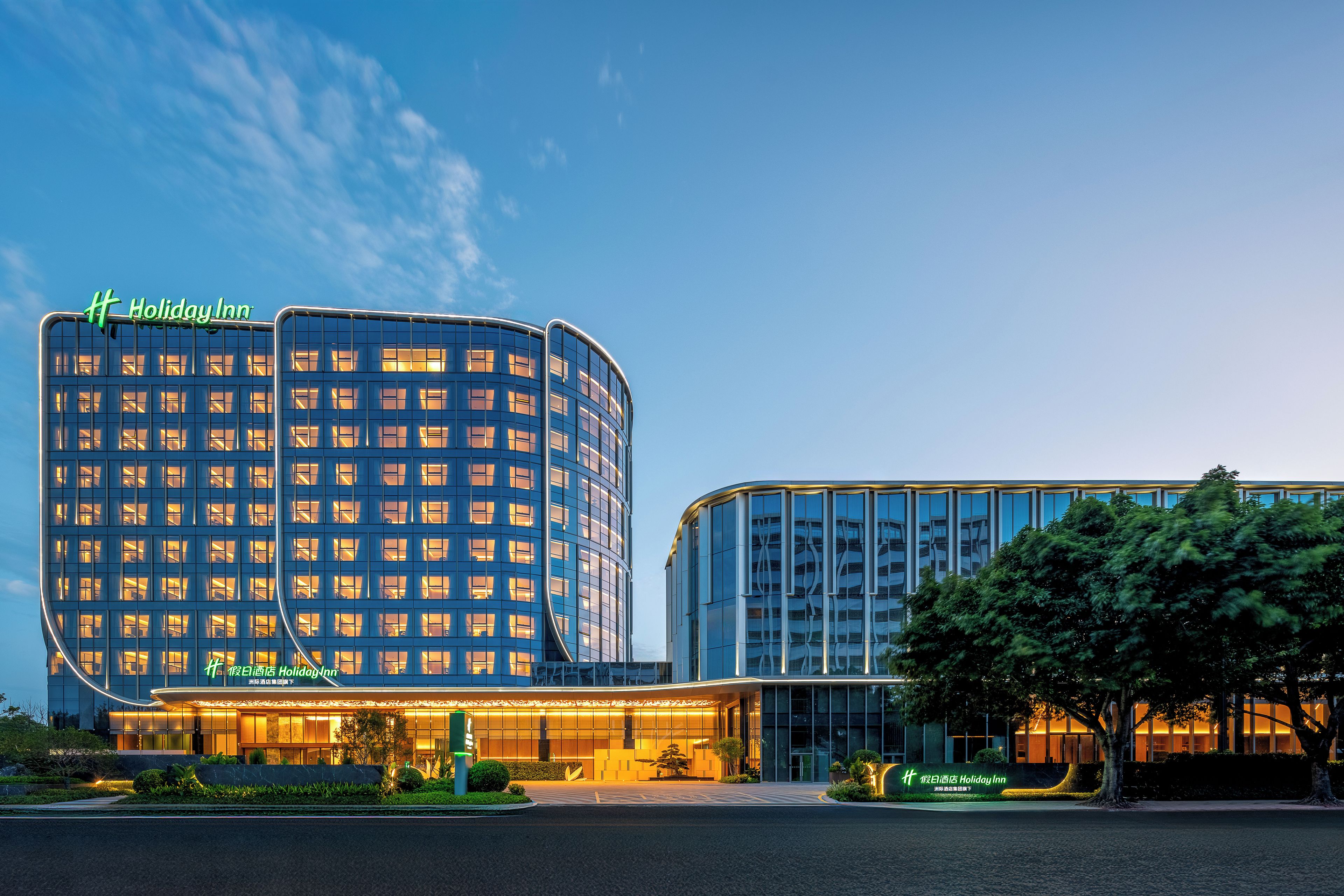 A modern Holiday Inn hotel with a curved facade, large windows, and a well-lit entrance.