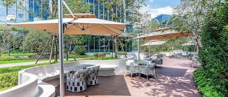 An outdoor patio area with seating and umbrellas, surrounded by greenery and modern buildings.