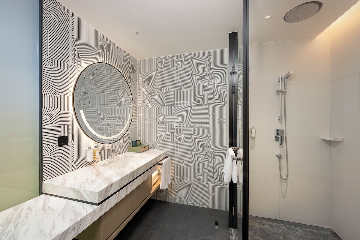 A modern bathroom with a marble sink, a large mirror, and a shower with a handheld showerhead.