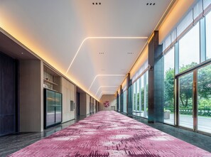 Un couloir moderne avec un tapis rose, de grandes fenêtres et un plafond doté d’un système d’éclairage linéaire.
