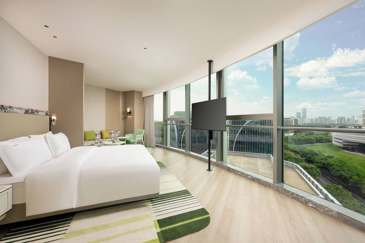 A modern hotel room with a large bed, a TV, and a balcony with a city view.