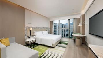 Een moderne hotelkamer met een groot bed, een zithoek met een bank en fauteuil, een eettafeltje en een grote televisie.