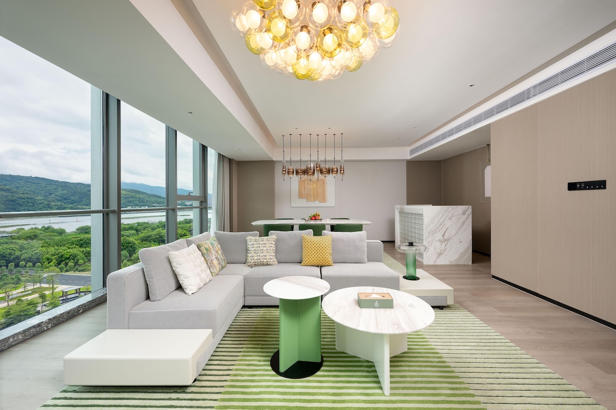 A modern living room with a large window, a green and white sofa, a white coffee table, and a unique chandelier.