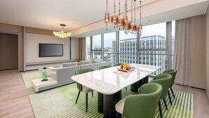A modern living room with a large dining table, green chairs, a sofa, and a TV mounted on the wall. - Holiday Inn Fuzhou Exhibition Center (Fuzhou)