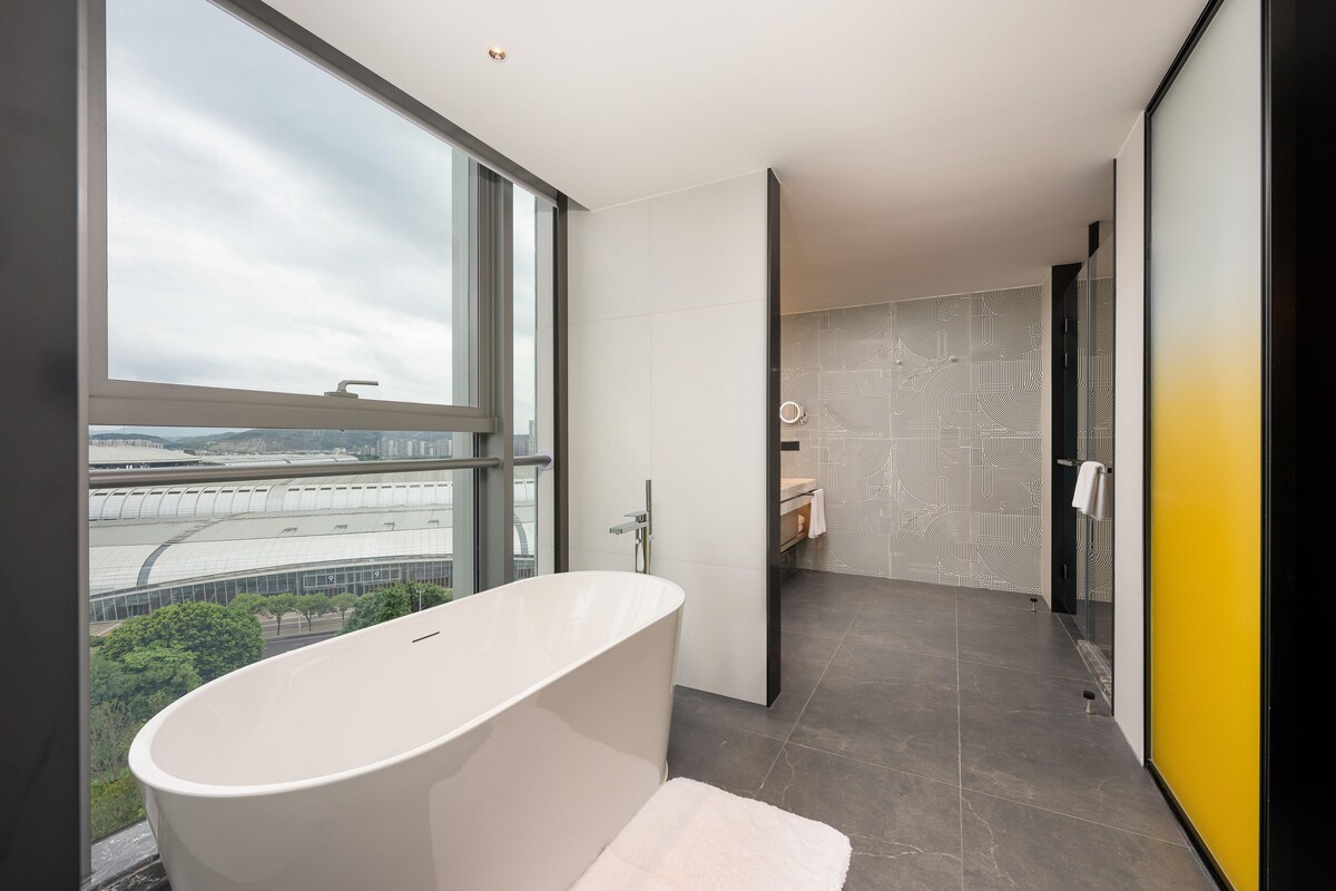 A modern bathroom with a freestanding bathtub, a large window, and a view of a stadium.