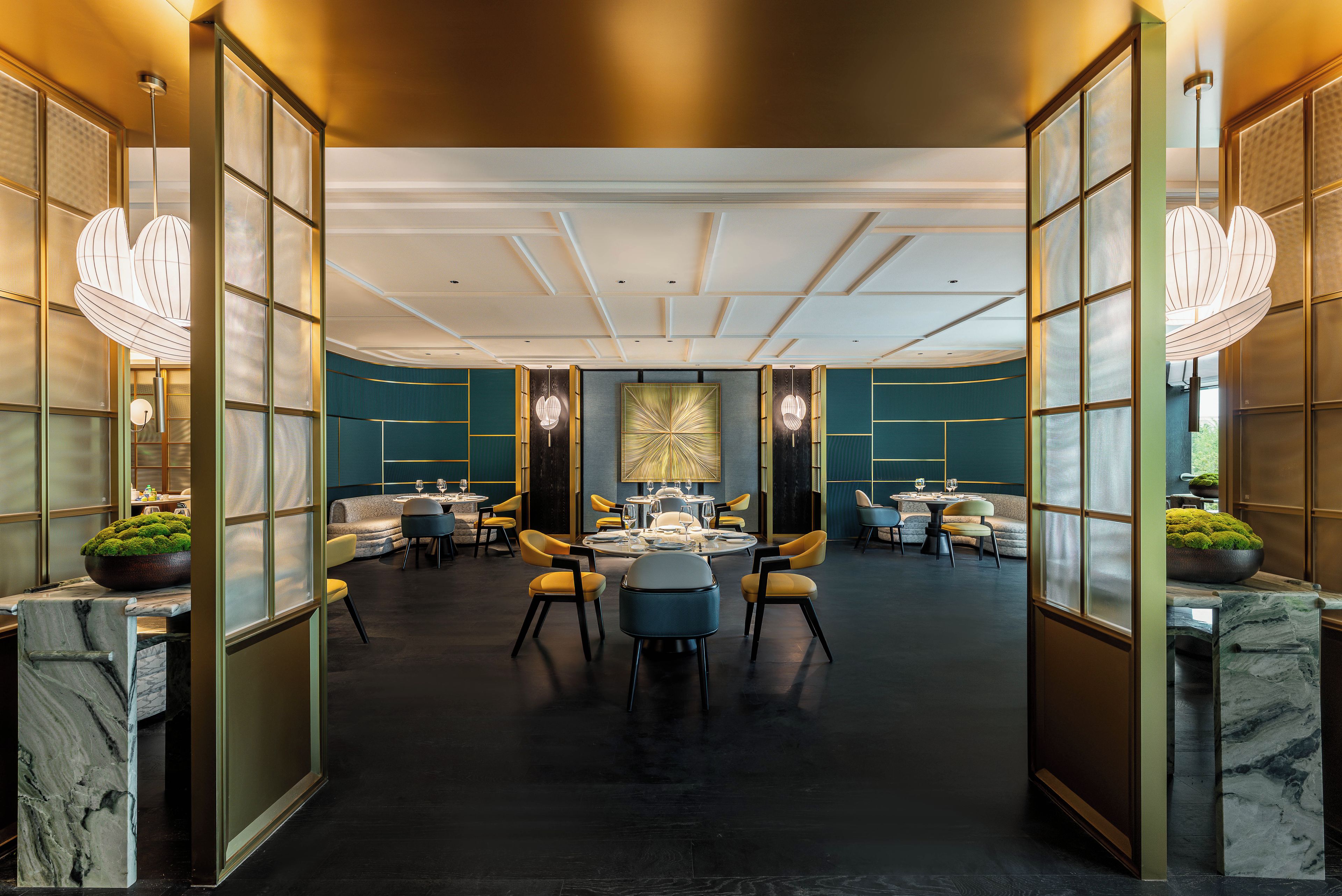 A spacious hotel lobby with a central round table, comfortable seating, and modern lighting fixtures.