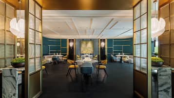 A spacious hotel lobby with a central round table, comfortable seating, and modern lighting fixtures.