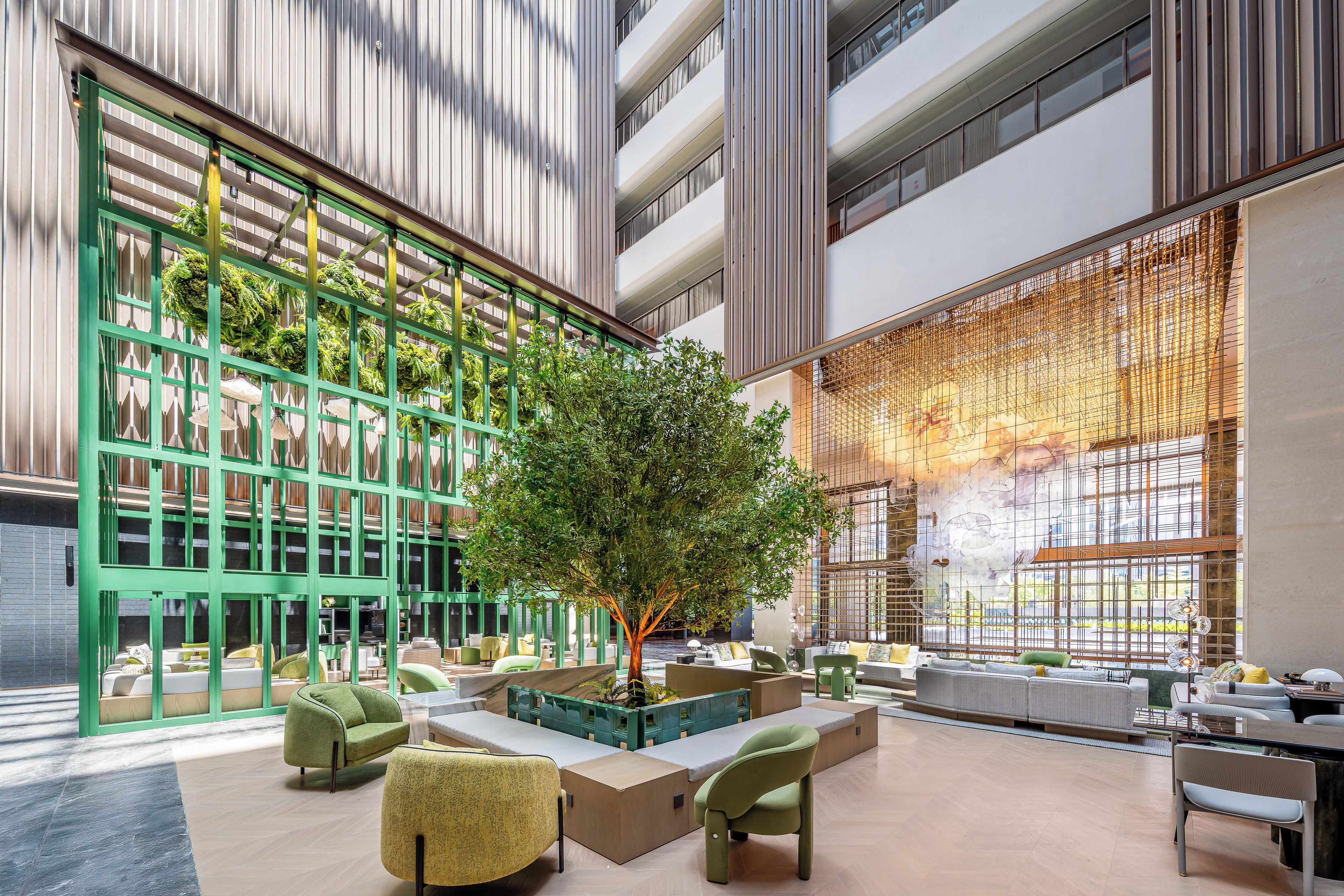 A spacious lobby with a central tree, seating areas, and a large window with a view.