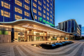 A modern hotel with a curved facade, illuminated signage, and a water feature in front. - Holiday Inn Fuzhou Exhibition Center (Fuzhou)