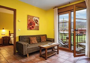A room with a sofa, a table, a painting, and a sliding glass door to an outdoor area. - Apartamentos Rurales La Viña (Cangas de Onis)