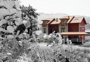 A two-story building with a red facade and terracotta roof tiles. - Apartamentos Rurales La Viña (Cangas de Onis)