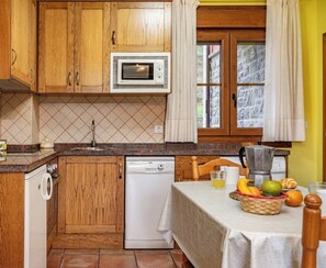 A kitchen with wooden cabinets, a microwave, a dishwasher, and a table with fruits and a coffee maker.
