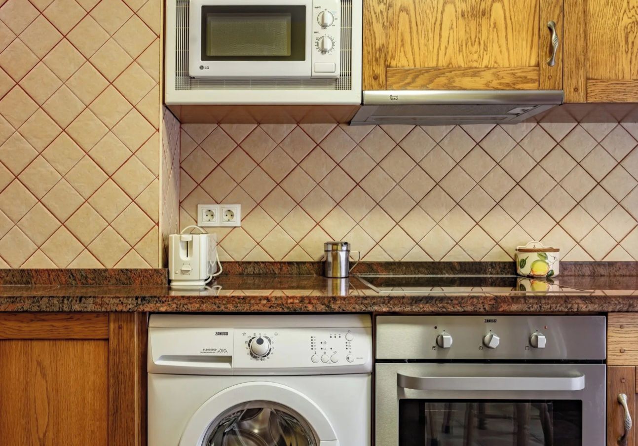 A kitchen with a microwave, toaster, kettle, washing machine, and oven.