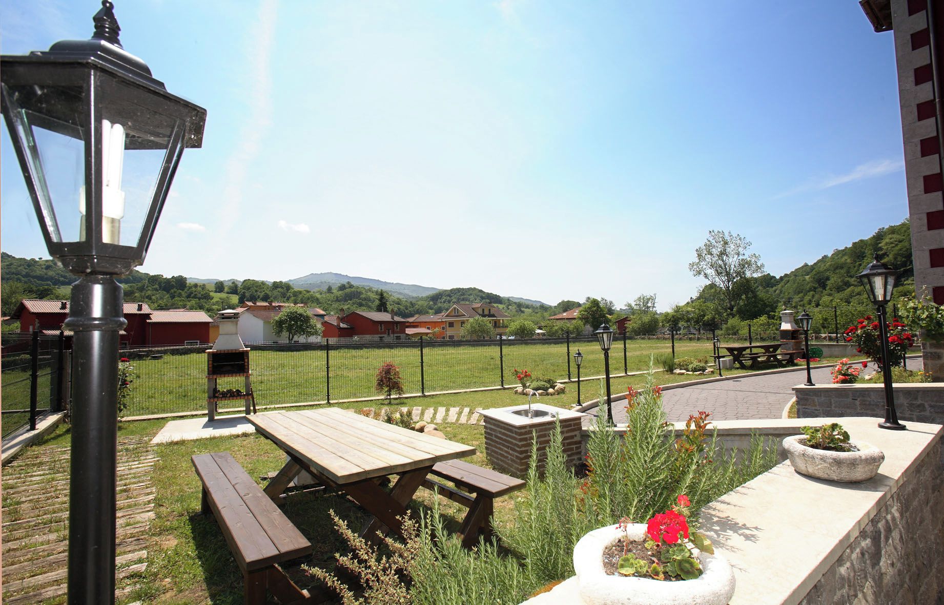 Un espace extérieur aménagé avec des tables de pique-nique, un barbecue et un bac en pierre rempli de fleurs.