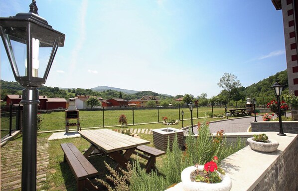 A patio area with picnic tables, a barbecue grill, and a stone planter with flowers.