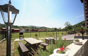 A patio area with picnic tables, a barbecue grill, and a stone planter with flowers. - Apartamentos Rurales La Viña (Cangas de Onis)