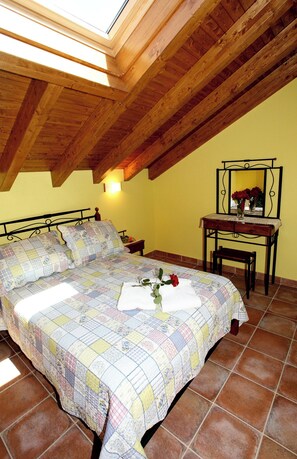 A bedroom with a wooden ceiling, a bed with a quilt, a bedside table with a lamp, and a mirror on the wall. - Apartamentos Rurales La Viña (Cangas de Onis)