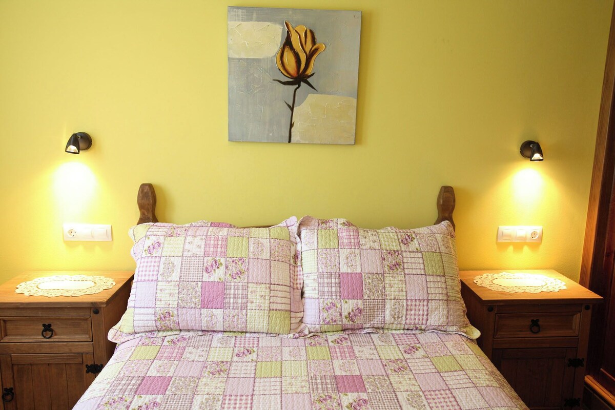 A bed with a floral quilt, two bedside tables with lamps, and a wall-mounted painting.