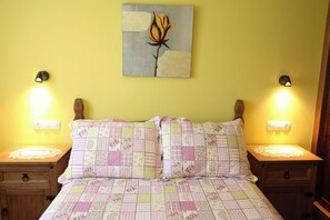 A bed with a floral quilt, two bedside tables with lamps, and a wall-mounted painting. - Apartamentos Rurales La Viña (Cangas de Onis)