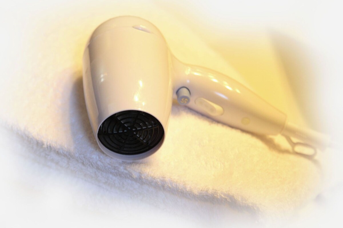 A white hair dryer with a black nozzle on a white towel.
