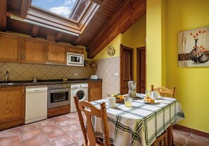 A kitchen with wooden cabinets, a microwave, a washing machine, and a dining table with a plaid tablecloth. - Apartamentos Rurales La Viña (Cangas de Onis)