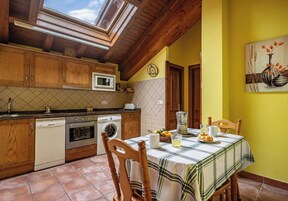 Una cocina con armarios de madera, microondas, lavadora y una mesa de comedor con mantel a cuadros.