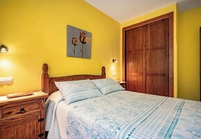Un dormitorio con una cama de madera, una mesita de noche, una lámpara de pared y una puerta.