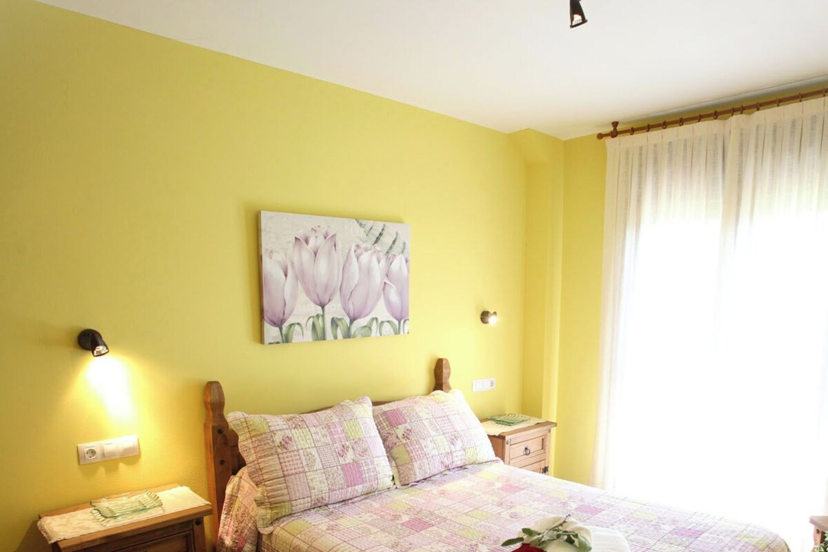 Een slaapkamer met een bed, nachtkastje, een raam met gordijnen en een plafondventilator.