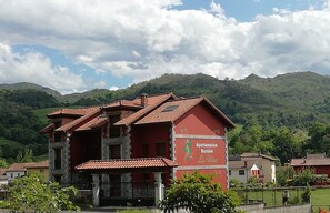 A red building with a sign reading 'Apartamentos Rurales La Vina' in front of a mountainous landscape. - Apartamentos Rurales La Viña (Cangas de Onis)