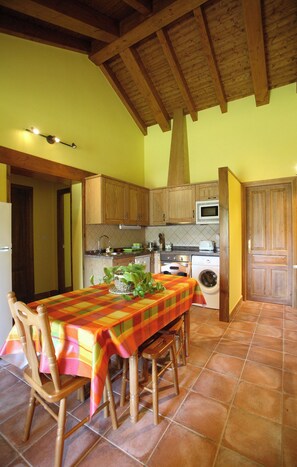 A kitchen with wooden cabinets, a microwave, a washing machine, and a dining table with chairs.