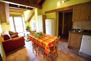 A cozy kitchen with wooden cabinets, a dining table with a colorful tablecloth, and a red sofa with patterned cushions. - Apartamentos Rurales La Viña (Cangas de Onis)