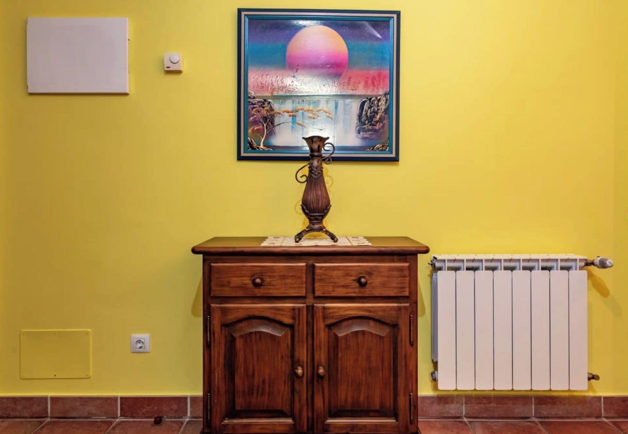 Een kamer met een houten kast, een radiator en een schilderij aan de muur.