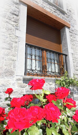 A stone building with a window featuring a wooden shutter and decorative metal bars. - Apartamentos Rurales La Viña (Cangas de Onis)