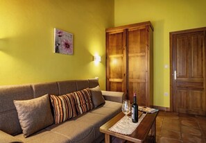 A room with a sofa, a wooden cabinet, a table with a bottle and glass, and a wall-mounted light.