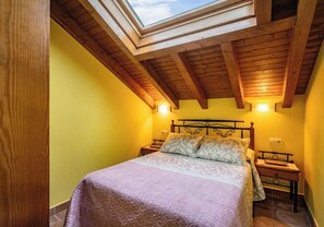 Un dormitorio con tragaluz, vigas de madera, una cama con ropa de cama estampada y mesitas de noche.