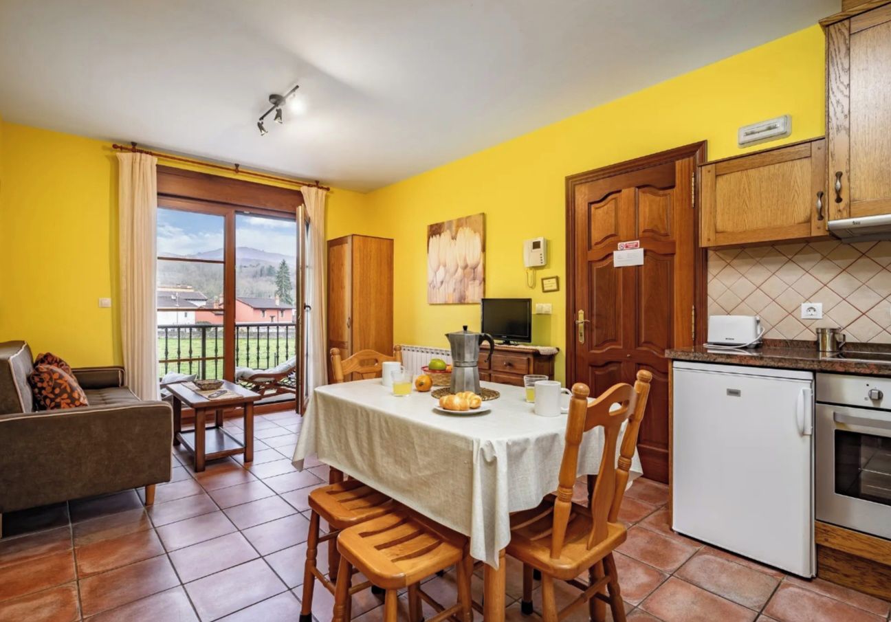 A dining area with a table set for four, a sofa, a refrigerator, and a kitchen counter.